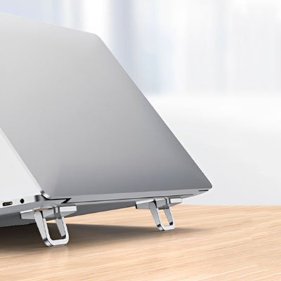 Support bureau pour ordinateur portable pliable en aluminium installé sous un ordinateur portable. Son design compact et ergonomique surélÚve l'écran pour améliorer la posture, réduire les douleurs cervicales et lombaires, tout en favorisant une meilleure circulation de l'air afin de limiter la surchauffe de l'appareil. Idéal pour le télétravail, le bureau et les déplacements.