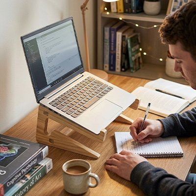 homme qui prend des note dans un calepin devant son ordinateur posé sur un Support bureau ordinateur portable 