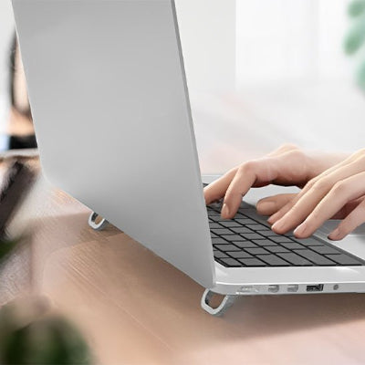 Support bureau pour ordinateur portable pliable en aluminium installé sous un ordinateur portable. Son design compact et ergonomique surélève l'écran pour améliorer la posture, réduire les douleurs cervicales et lombaires, tout en favorisant une meilleure circulation de l'air afin de limiter la surchauffe de l'appareil. Idéal pour le télétravail, le bureau et les déplacements.