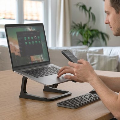 un homme travail a son bureau sur un ordinatuer portable posé sur un support pc portable noir
