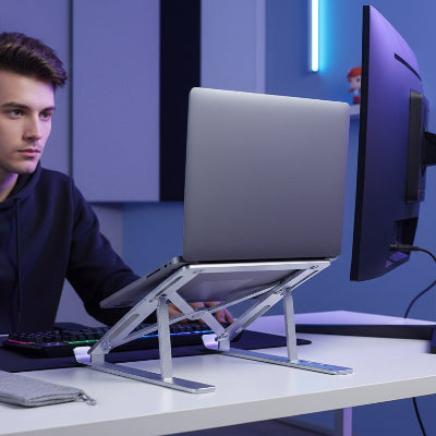 jeune homme a son bureau avec un portable posé sur un Support pc portable et un écran sur son bureau 